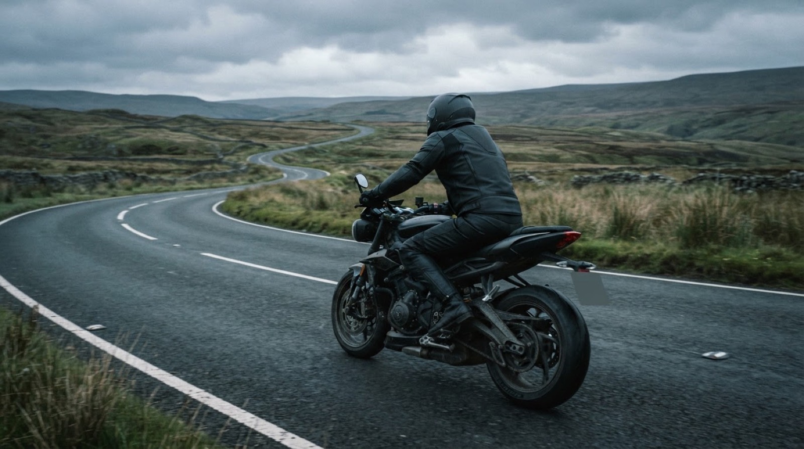 A motorcyclist riding a sweeping British A-road across open moorland